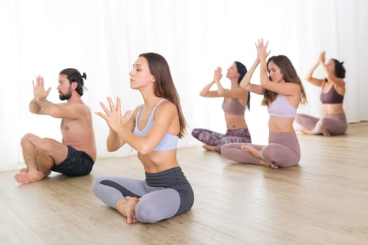 Group of young authentic sporty attractive people in yoga studio, practicing yoga lesson with instructor. Healthy active lifestyle, working out in gym.