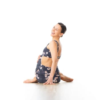 Rear view of young sporty female yoga instructor in bright white yoga studio, smiling cheerfully while looking in camera