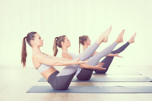 Group of young sporty attractive women in yoga studio, practicing yoga lesson with instructor, forming a line in Navasana, boat asana yoga pose. Healthy active lifestyle, working out indoors in gym.