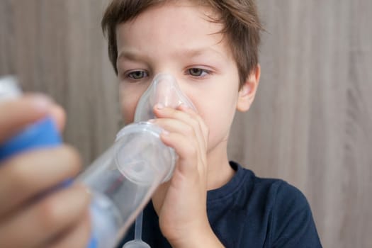 Child boy using medical spray for breath. Inhaler, spacer and mask. Side view
