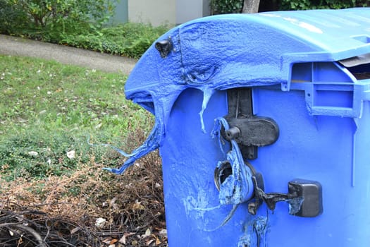 A blue waste paper container was burned by vandalism. The plastic has melted. Arson is a criminal offense.