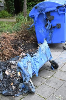 A blue waste paper container was burned by vandalism. The plastic has melted. Arson is a criminal offense.