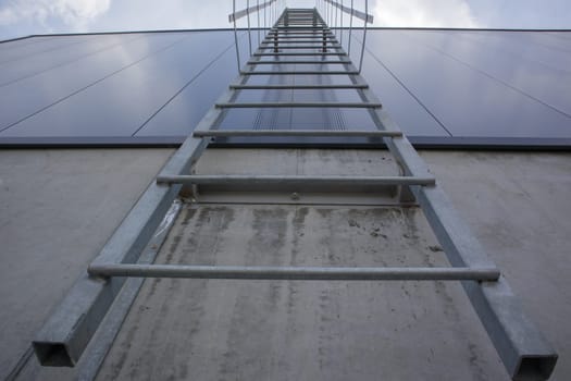 Fire escape on the industrial building above, bottom view. Stainless steel handrails, roof ladder. Detail view of stairs with safety cage. Building construction concept