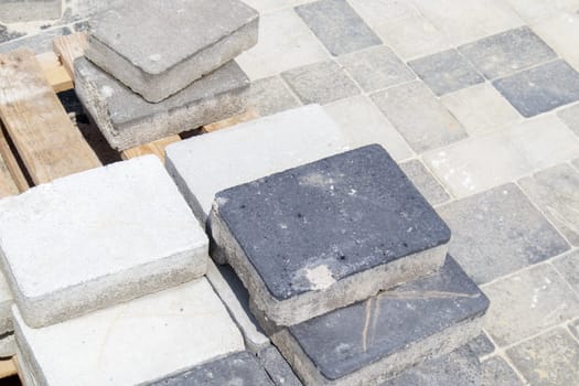 Concrete or paved gray paving slabs or floor or walkway stones stacked on a pallet. Concrete paving slabs in the backyard or road paving. Garden brick path in the courtyard on a sandy foundation