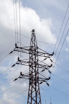 High voltage electrical tower. Power lines and power pylons on a sunny day with circular clouds in the blue sky. High voltage power transmission line supports. They have a complex steel structure