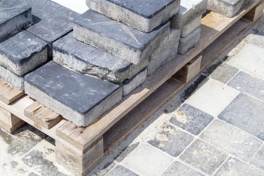 Concrete or paved gray paving slabs or floor or walkway stones stacked on a pallet. Concrete paving slabs in the backyard or road paving. Garden brick path in the courtyard on a sandy foundation