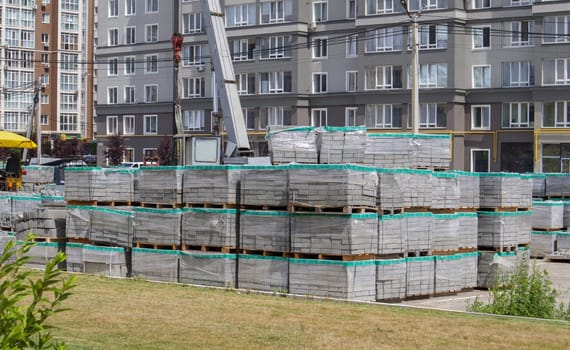 There are many new gray paving slabs on plastic-covered pallets on the construction site. Paving of pedestrian paths on a city street. Foreground. Repair of the sidewalk in the city square