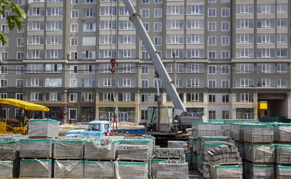 There are many new gray paving slabs on plastic-covered pallets on the construction site. Paving of pedestrian paths on a city street. Foreground. Repair of the sidewalk in the city square