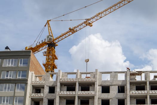 Construction crane on an unfinished residential building against the sun and blue sky. Housing construction, apartment building in the city. Construction site of residential buildings