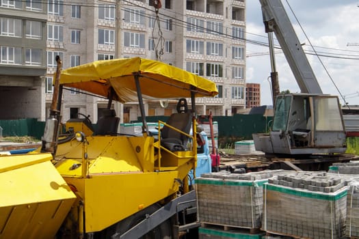 An asphalt paver is parked at a construction site. Road construction machinery stands by the road in a warehouse. Construction of heavy roads and repair of city streets