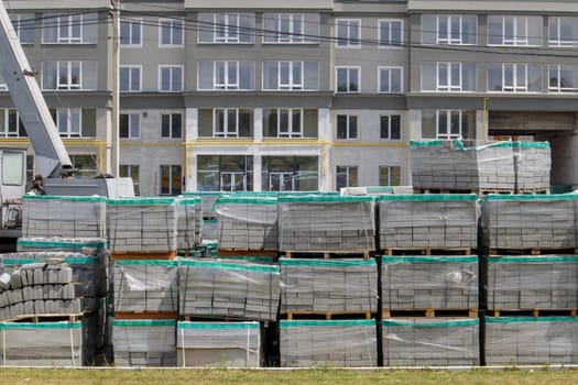 There are a lot of new gray paving slabs on the construction site on plastic-covered pallets. Paving of pedestrian paths on a city street. Ukraine, Kiev - August 19, 2021