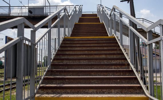 Railway bridge with steps, with impressive steps in perspective. Overhead pedestrian crossing. Bridge stairs connecting one platform to another at the train station. Ukraine, Kiev - August 19, 2021