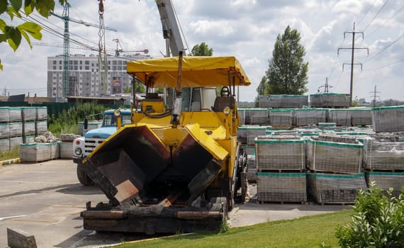An asphalt paver is parked at the construction site. Road construction equipment stands by the road in a warehouse. Heavy road construction and street repair. Ukraine, Kiev - August 19, 2021