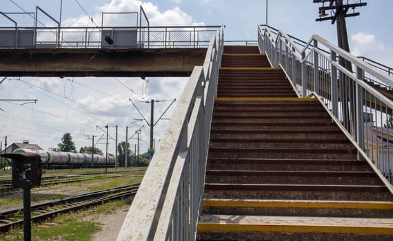Railway bridge with steps, with impressive steps in perspective. Overhead pedestrian crossing. Bridge stairs connecting one platform to another at the train station. Ukraine, Kiev - August 19, 2021