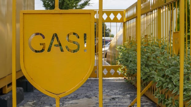 Warning on a metal cage with gas equipment for the public. Attention gas pipe. The inscription in English GAZ. A yellow warning sign for a medium pressure gas pipeline on a surface installation