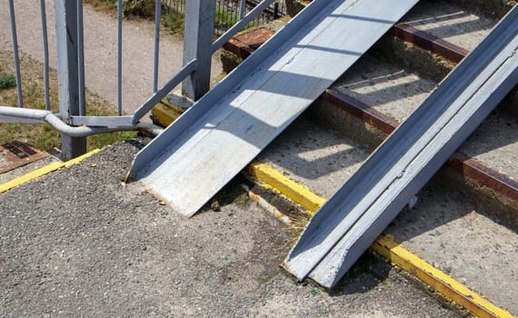 The staircase of the pedestrian crossing with traces of destruction. Two wheelchair rails. Metal railings for bicycles, wheelchairs and strollers with children. Special equipment on the stairs
