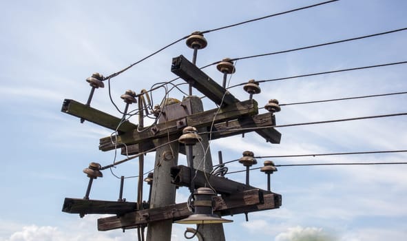 Wooden electric pole with high voltage wires close-up. Pillar against the blue sky. Old decrepit wooden telephone pole against the blue sky