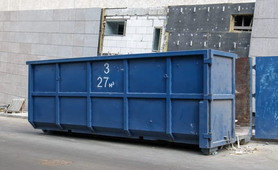 Metal durable blue industrial trash bin for outdoor trash at construction site. Large waste basket for household or industrial waste. A pile of waste