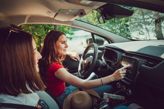 Two young girls listening to good music while driving in car, enjoy summer road trip in nature.