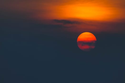 Beautiful sunset. Dramatic Fiery Sun Surrounded by Clouds During Sunset.  Vibrant orange red clouds are back lit by the sun.