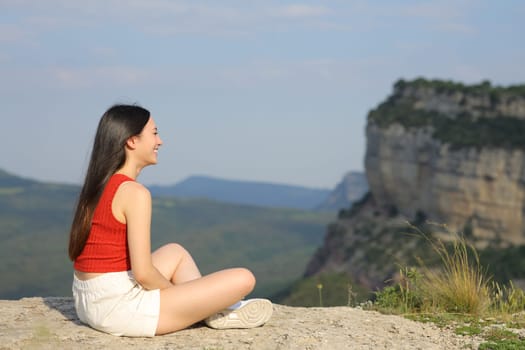 Full body portrait of an asian woman contemplating views sitting in a mountain cliff