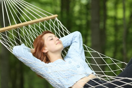 Woman relaxing lying on rope hammock in a forest on summer vacation