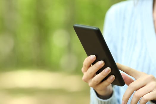 Close up of a woman hands using smart phone walking in a forest