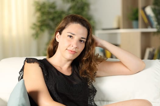 Serious woman posing looking at camera sitting on a couch in the living room at home