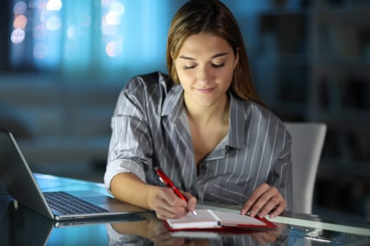 Satisfied woman writing on paper agenda on a table in the night at home
