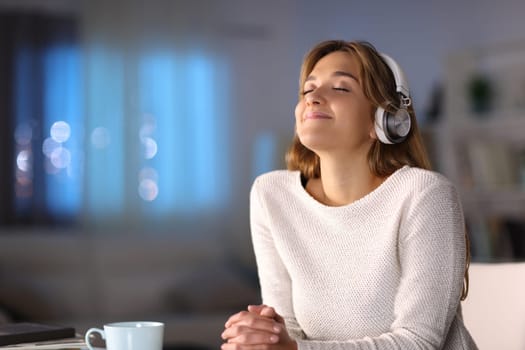 Woman wearing wireless headphones relaxing listening to music at home in the night