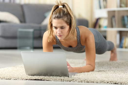 Full body portrait of a woman practicing sport watching video tutorials on laptop at home