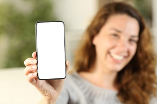 Happy housewife showing phone screen mock up sitting on a sofa in the living room at home