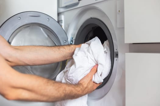 Housework: Man loading white clothes into washing machine