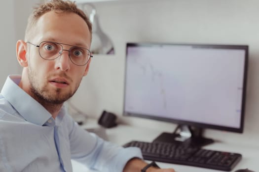 Portrait of surprised man in glasses and office shirt on background of monitor with graph of falling market. Stock market crisis. Cryptocurrency. Lottery, Winnings. Failure