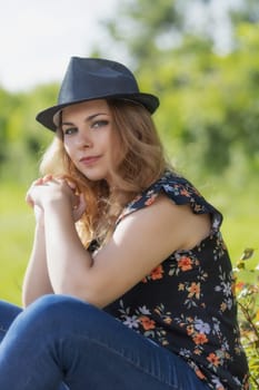 Cool young woman in straw hat is posing outdoors looking at the camera. Vertically.