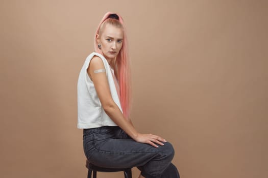 Young hipster woman with band aid after coronavirus Covid-19 vaccine injection. Covid vaccination concept, plain color background