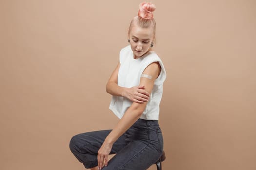 Young hipster woman with band aid after coronavirus Covid-19 vaccine injection. Covid vaccination concept, plain color background