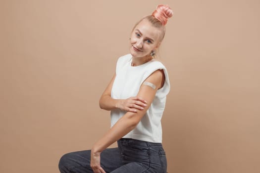 Young hipster woman with band aid after coronavirus Covid-19 vaccine injection. Covid vaccination concept, plain color background