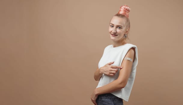 Young hipster woman with band aid after coronavirus Covid-19 vaccine injection. Covid vaccination concept, plain color background