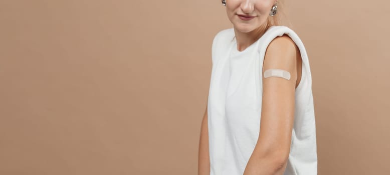 Young hipster woman with band aid after coronavirus Covid-19 vaccine injection. Covid vaccination concept, plain color background
