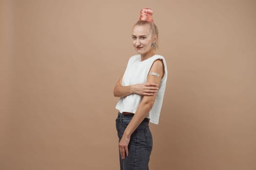 Young hipster woman with band aid after coronavirus Covid-19 vaccine injection. Covid vaccination concept, plain color background