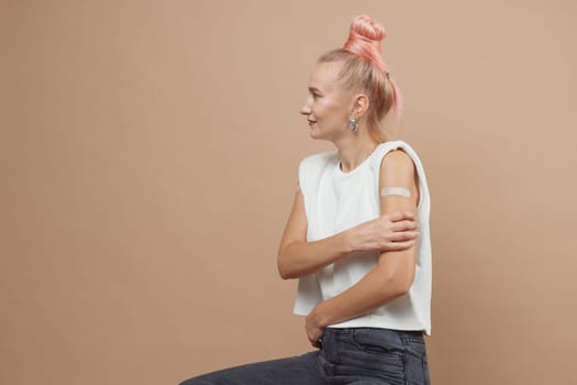 Young hipster woman with band aid after coronavirus Covid-19 vaccine injection. Covid vaccination concept, plain color background