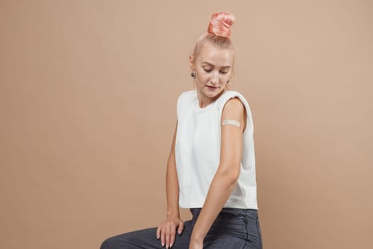 Young hipster woman with band aid after coronavirus Covid-19 vaccine injection. Covid vaccination concept, plain color background