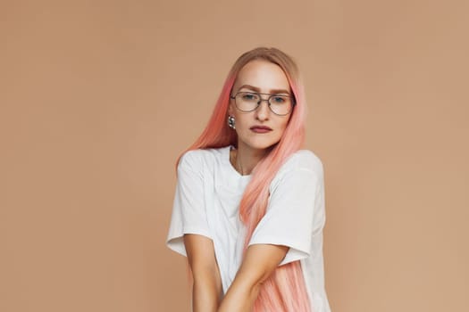 Young beautiful woman with pink hair in white t-shirt, wearing eyeglasses. Portrait. Beige background. Girl looking at camera.