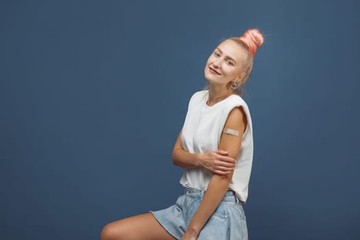 Young hipster woman with band aid after coronavirus Covid-19 vaccine injection. Covid vaccination concept, plain color background