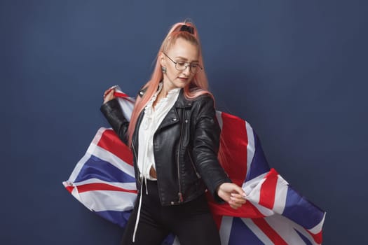 Young woman expat in eyeglasses with great britain flag. Studio shot. English language hipster teacher. Fashionly dressed woman with pink hairs in black leaher jacket and white blouse. Autumn style