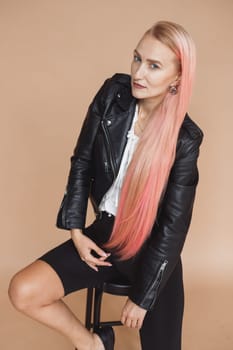 Beautiful blonde girl in black leather jacket and pink hair in rock style on plain background