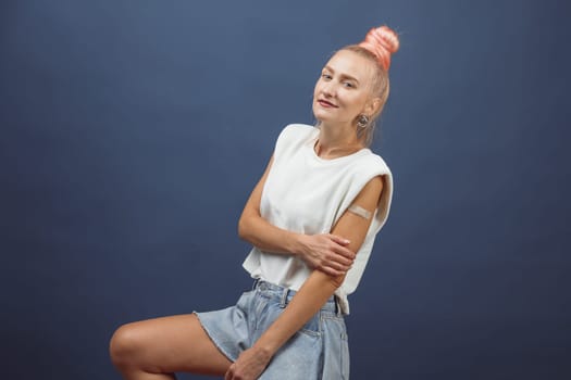 Young hipster woman with band aid after coronavirus Covid-19 vaccine injection. Covid vaccination concept, plain color background