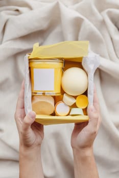 Female hands hold care box set of eco - friendly cosmetics. Bath salt, scrub, handmade soap, washing sponge on textile background. Top view. Concept animal fat free, zero waste.