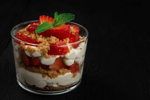 Strawberry with cookie and cream dessert decorated with mint leaf on black wooden background, with copyspace